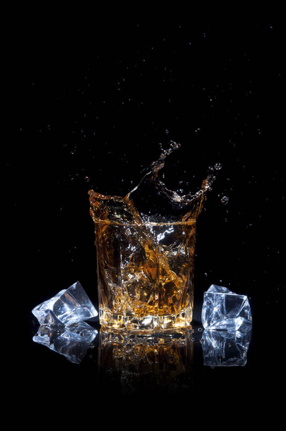 Whiskey with splash and ice, isolated on black background. Alcoholic beverage with splash. - Foto, afbeelding