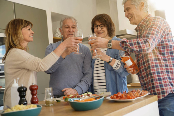 Senior people cheering with wine while preparing meal - Photo, image