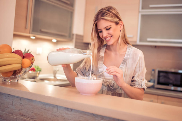 lächelnde junge Frau frühstückt in der Küche und isst Cornflakes. - Foto, Bild