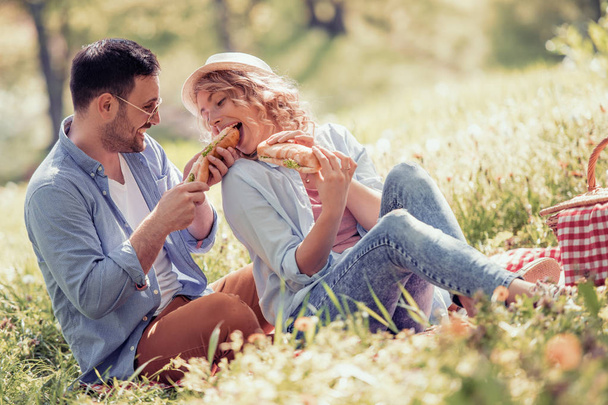 Szczęśliwa para na piknik uśmiecha się do siebie w słoneczny dzień. Koncepcja ludzie, miłość, szczęście i Natura. - Zdjęcie, obraz