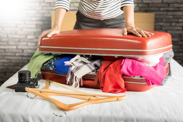 Woman trying to fit all clothing to packing her red suitcase before vacation - Photo, Image