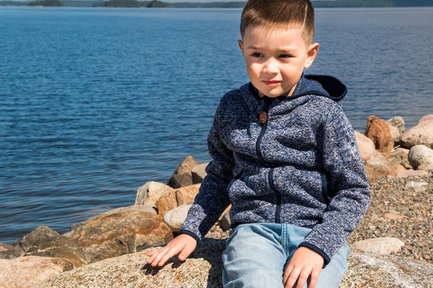Kid sits on a rocks near sea at Finland. Young handsome boy and nature, scandinavian look - Foto, Imagem
