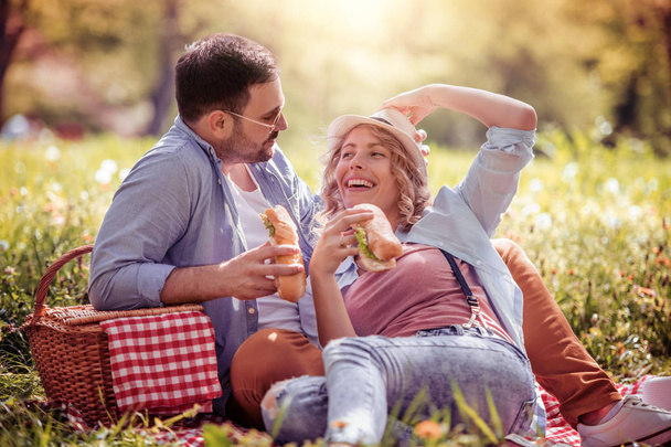 Onnellinen pari piknikillä hymyilemässä toisilleen aurinkoisena päivänä.Ihmiset, rakkaus, onnellisuus ja luonto käsite
. - Valokuva, kuva