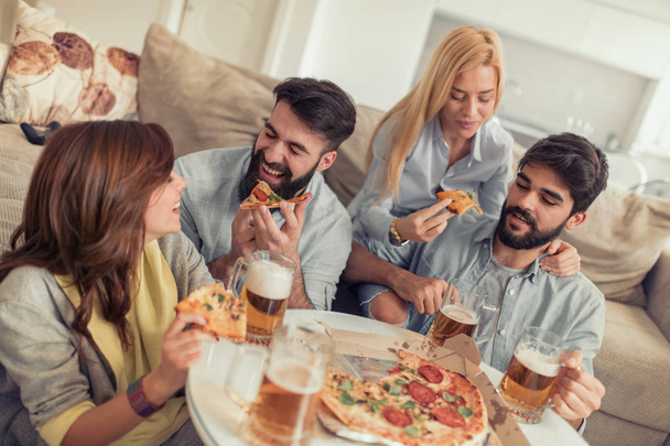 Улыбающиеся друзья едят пиццу и пьют пиво дома
 - Фото, изображение