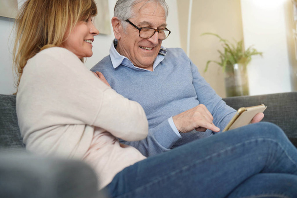 Senior couple in sofa websurfing on digital tablet - Фото, изображение
