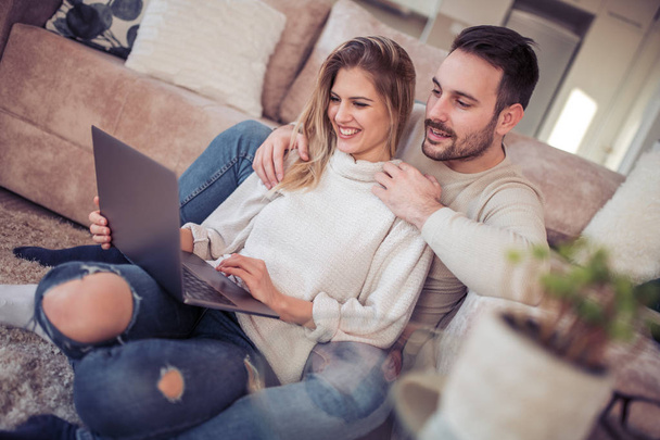 Joyeux jeune couple passer du temps ensemble à la maison, en utilisant un ordinateur portable
. - Photo, image