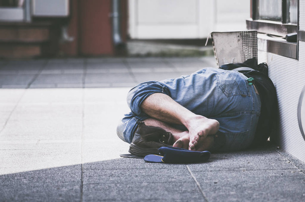Homeless or drunk man sleeps on the street in the shadow of the building barefooted  - Photo, Image