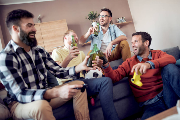 Mladí přátelé odpočívá s lahví nápoje, mluví o fotbale a usmívá se. - Fotografie, Obrázek
