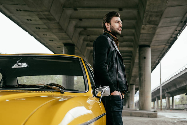 widok boczny stylowy mężczyzna stojący w pobliżu żółty samochód retro i szukasz drogi - Zdjęcie, obraz