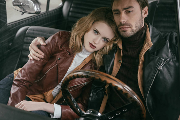 beautiful stylish young couple in leather jackets embracing in retro car - Photo, image