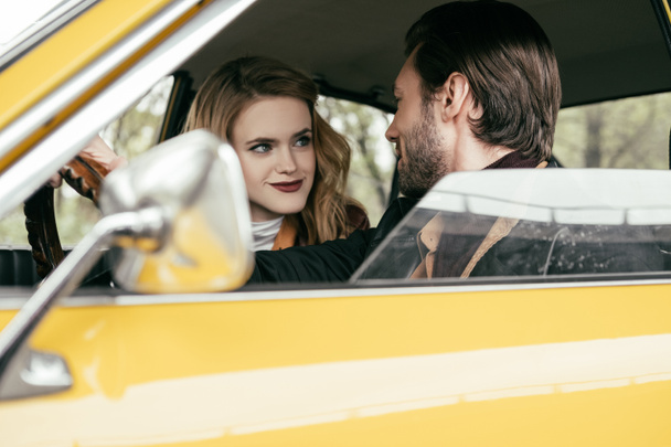 hermosa pareja joven con estilo sonriendo entre sí mientras se sientan juntos en el coche
 - Foto, imagen