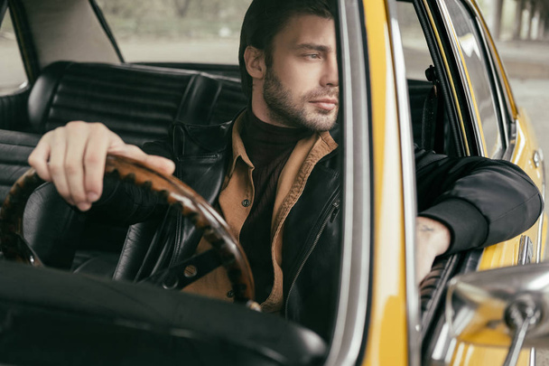 zamyślony przystojny stylowy człowiek siedzi w retro samochód i szukasz drogi  - Zdjęcie, obraz