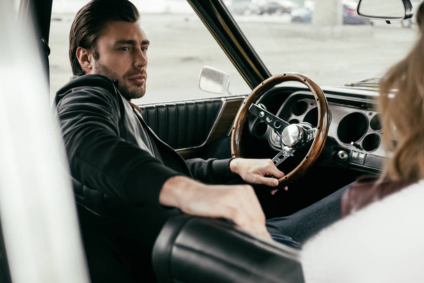 handsome stylish young man looking away while sitting in old-fashioned car - Fotoğraf, Görsel