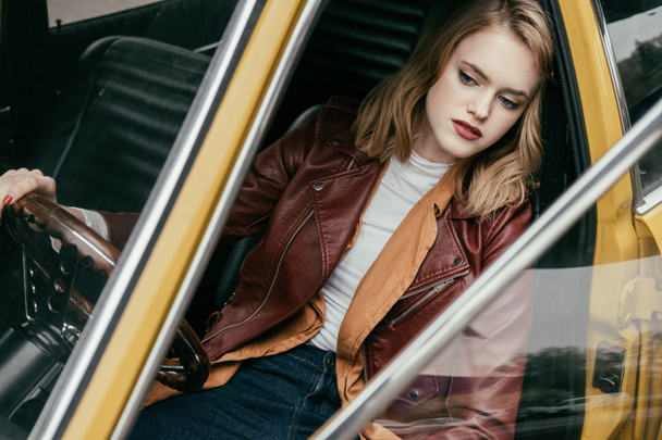 high angle view of girl in leather jacket sitting in retro car and looking away - Fotó, kép