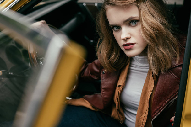 beautiful stylish young woman sitting in old-fashioned car and looking at camera - Foto, imagen
