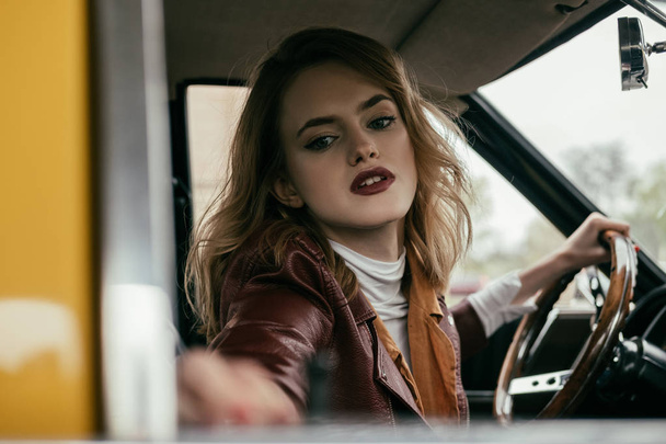 selective focus of attractive girl holding steering wheel of classic car - Zdjęcie, obraz