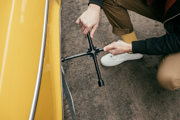 cropped shot of man in leather jacket fixing wheel of yellow vintage car  - Photo, Image