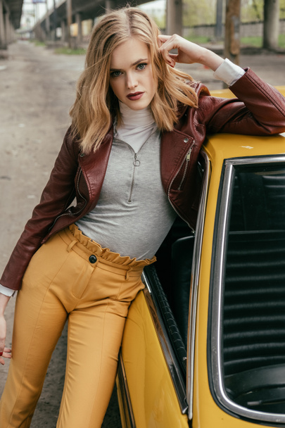 beautiful stylish young woman leaning at yellow car and looking at camera - Fotoğraf, Görsel