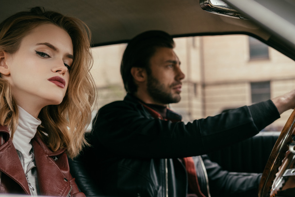 attractive stylish girl looking at camera while handsome boyfriend driving car  - Foto, imagen