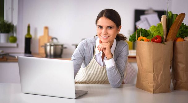 Beautiful young woman cooking looking at laptop screen with receipt in the kitchen - Foto, imagen