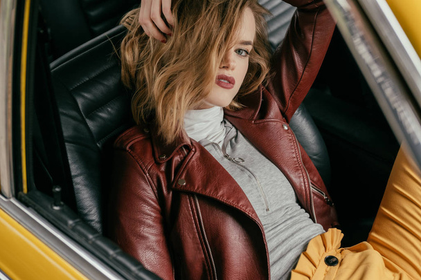 high angle view of stylish girl sitting in retro car and looking at camera  - Foto, imagen
