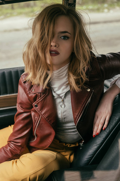 seductive girl in leather jacket looking at camera while sitting in car     - Zdjęcie, obraz