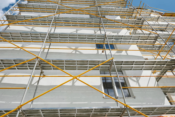 Σκαλωσιές κοντά σε ένα νέο σπίτι, το κτήριο εξωτερικά, βιομηχανία κατασκευής και επισκευής, λευκό τοίχο και παράθυρο, κίτρινο σωλήνα - Φωτογραφία, εικόνα
