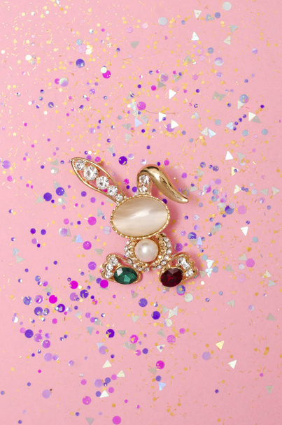 Lapin broche doré avec diamants et pierre de lune en paillettes isolées sur fond rose
 - Photo, image