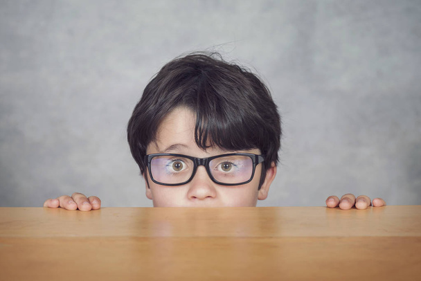 boy with glasses on a wooden table on gray background - Foto, Imagen