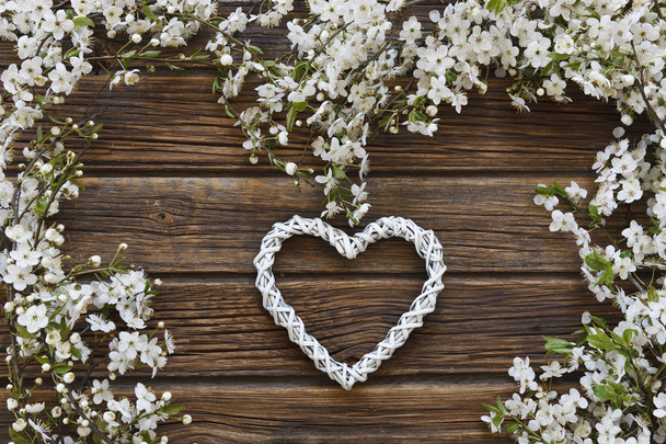 Close-up photo of Beautiful white Flowering Cherry Tree branches with white heart shape. Wedding, engagement or betrothal concept on vintage wooden background. Top view, greeting card.  - Fotó, kép