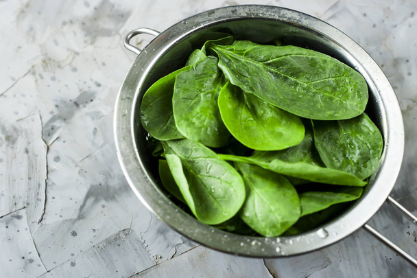 Washed spinach in a metal colander on a gray background. Fresh green leaves for cooking healthy dishes - Photo, Image