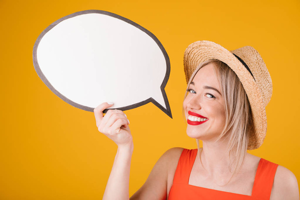 Attractive blonde smiling girlin straw hat and red fancy dress is holding speech buble banners. Yellow background - 写真・画像