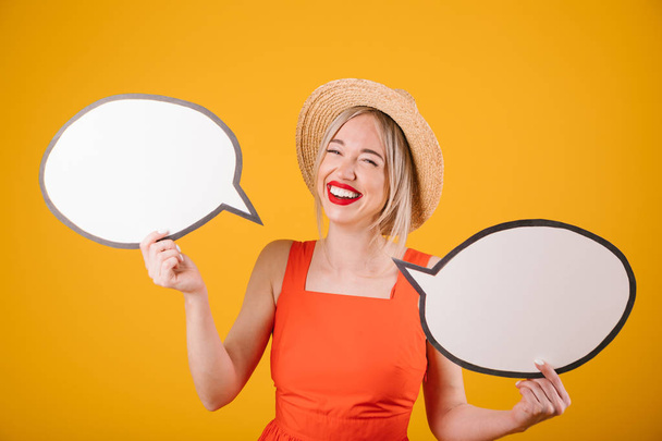 laughing adorable blonde girl in straw hat and red fancy dress is holding speech buble banners. Yellow background - Φωτογραφία, εικόνα