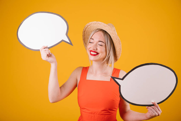 Happy lovely blonde girl in straw hat and red fancy dress is holding speech buble banners. Yellow background - Фото, изображение