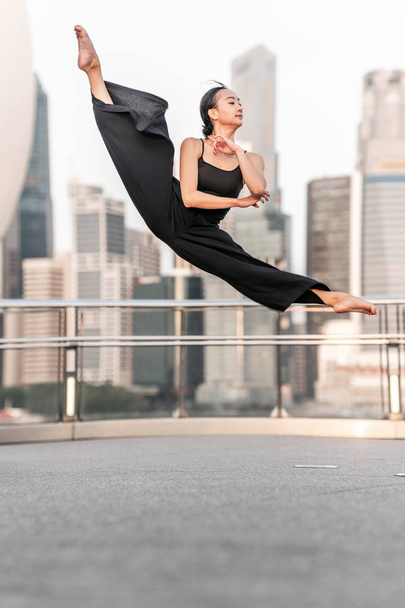 Cute Young woman athlete performs a perfect leap high up, on a bridge  with background of skyscrapers  - Foto, imagen