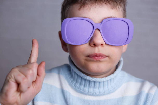 Cute boy in violet sunglasses with opaque lenses pointing upward - Φωτογραφία, εικόνα