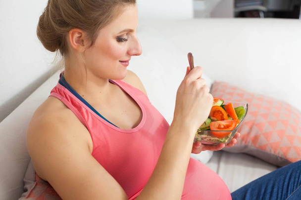 Fiatal szép terhes nő étkezési növényi saláta. A lány a gazdaság egy tál saláta. Az egészséges táplálkozás. Terhesség. Anyaság. Egészségügyi. - Fotó, kép