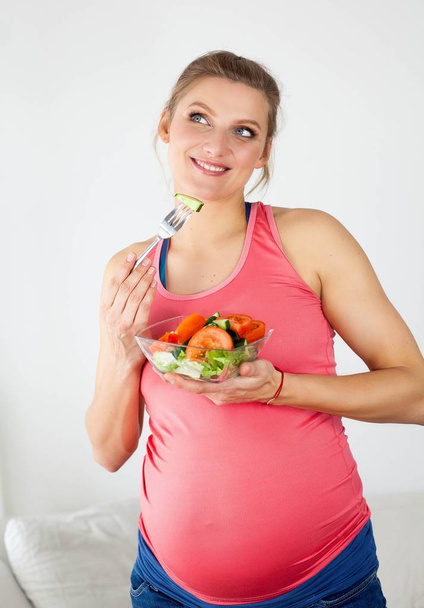 Giovane bella donna incinta sta mangiando insalata di verdure. La ragazza ha in mano un piatto di insalata. Note di alimentazione. Gravidanza. La maternità. Sanità
. - Foto, immagini