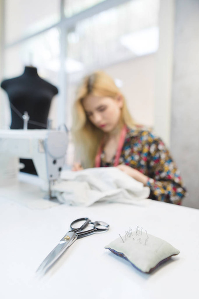Scissors and pillow with needles on the background of seamstresses working in the workplace. Work place for seamstresses. Sewing concept. Dressmaker work - Foto, afbeelding