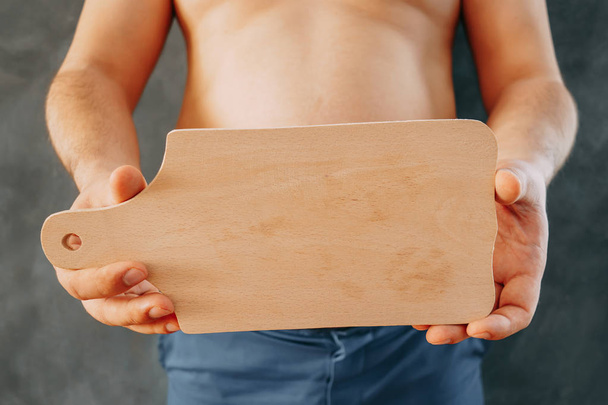 Overweight man holding empty chopping board in hands. Copy space - Fotografie, Obrázek