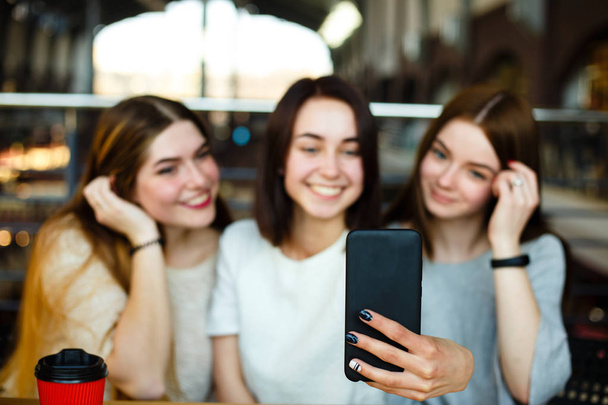 Three friends make selfie and drink coffee at cafe - Fotó, kép