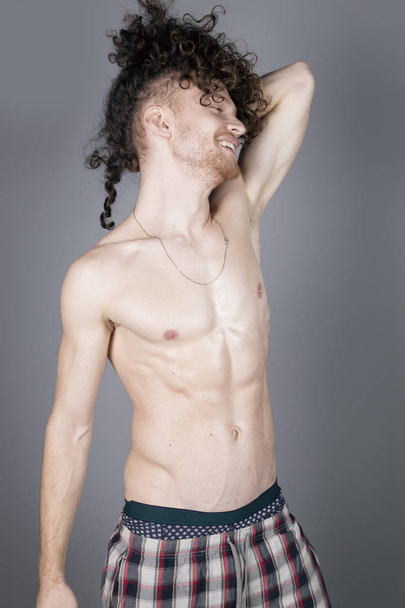 Attractive young man with long ginger curly hair posing with athletic body in pajamas, studio portrait - Valokuva, kuva