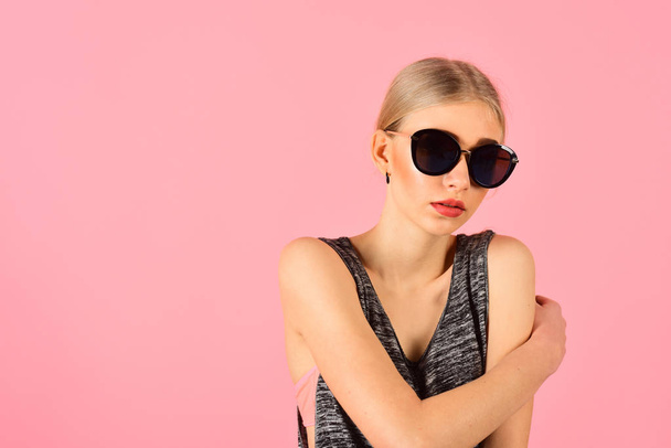 Closeup portrait of blond model with ponytail in melange gray sleeveless blouse wearing big black sunglasses isolated on pink background. Summer eyewear fashion. - Фото, изображение