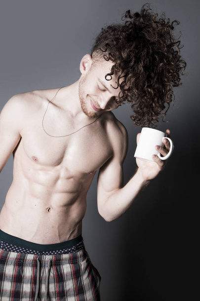 Attractive young man with long ginger curly hair having a cup of coffee or tea, studio portrait - Foto, immagini