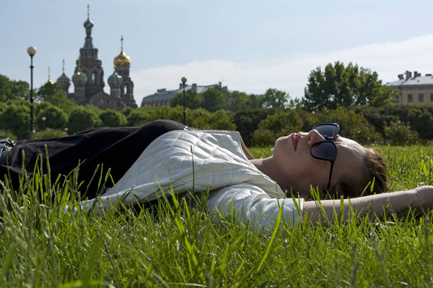 girl in a white jacket and sunglasses lying on the grass on the  - Valokuva, kuva