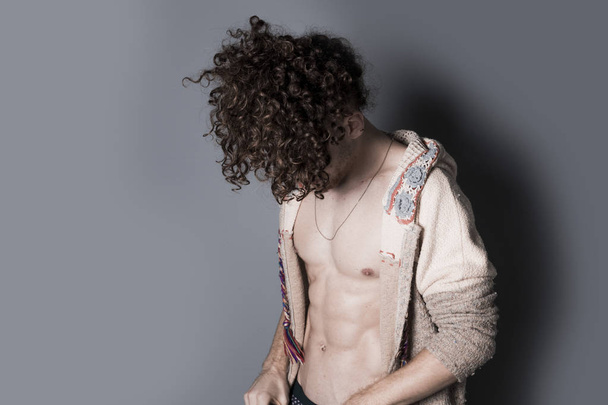 Attractive young man with long ginger curly hair posing with athletic body in pajamas and cardigan, studio portrait - Foto, imagen
