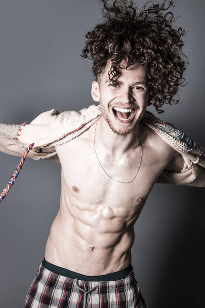 Attractive young man with long ginger curly hair posing with athletic body in pajamas and cardigan, studio portrait - Photo, Image