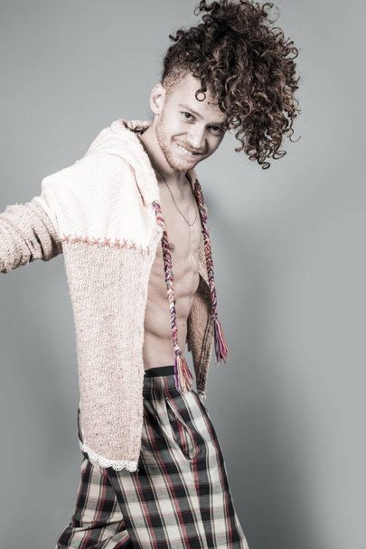 Attractive young man with long ginger curly hair posing with athletic body in pajamas and cardigan, studio portrait - Fotografie, Obrázek