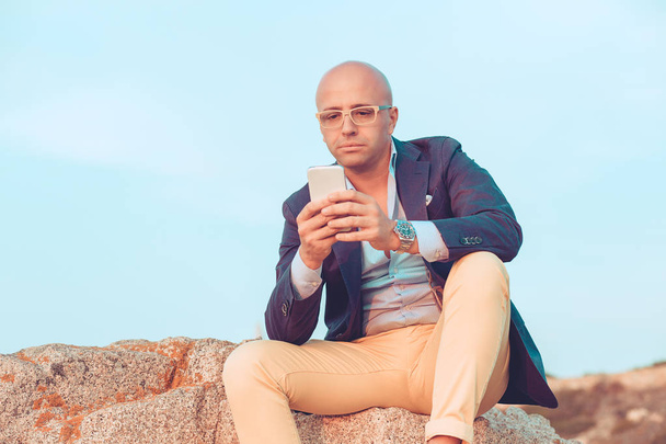 Confused trendy man with phone on rock - Foto, Imagem