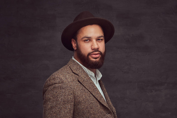 Retrato de estudio de un guapo hombre afroamericano con una elegante chaqueta marrón y sombrero
. - Foto, imagen